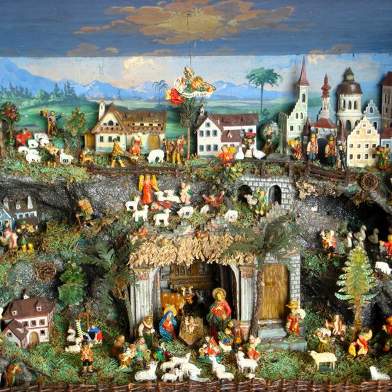 Eine detaillierte Miniatur-Krippenszene mit Figuren von Jesus, Maria und Josef, umgeben von Tieren und Hirten, in einer kleinen Dorflandschaft mit Häusern und einer Kirche.