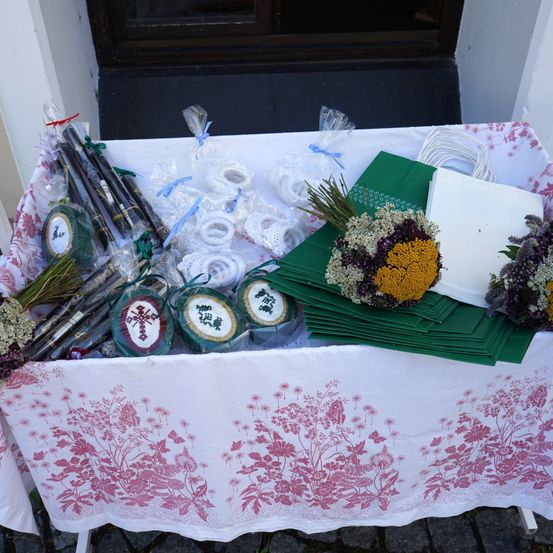 Ein Tisch mit einem Blumentischtuch zeigt eine Auswahl an Artikeln, darunter verpackte Süßigkeiten, Blumen und Servietten. Der Tisch steht vor einem Gebäude.