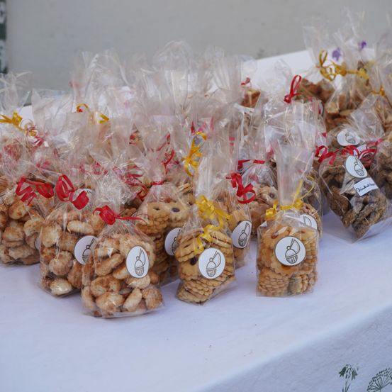 Ein Tisch voller durchsichtiger Plastiktüten, die jeweils eine Auswahl an Keksen enthalten, die mit bunten Schleifen gebunden sind. Die Kekse scheinen eine Mischung aus Schokoladenkeksen und Shortbread zu sein.
