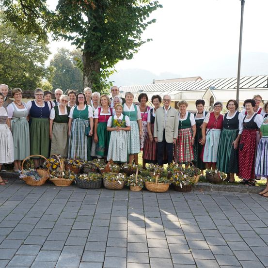 Eine Gruppe von Menschen in traditioneller Kleidung posiert für ein Foto mit Körben voller Blumen vor ihnen.