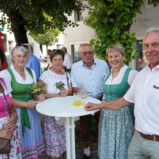 Eine Gruppe von Menschen, darunter drei Frauen und zwei Männer, stehen um einen Tisch mit Getränken und lächeln für ein Foto. Sie sind in traditioneller deutscher Kleidung gekleidet.
