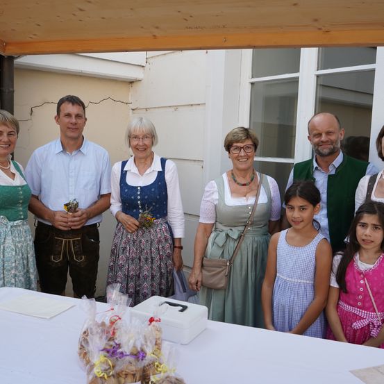 Eine Gruppe von Menschen, einschließlich Erwachsener und Kindern, steht lächelnd zusammen vor einem Tisch mit Essen. Sie scheinen bei einer Veranstaltung zu sein.