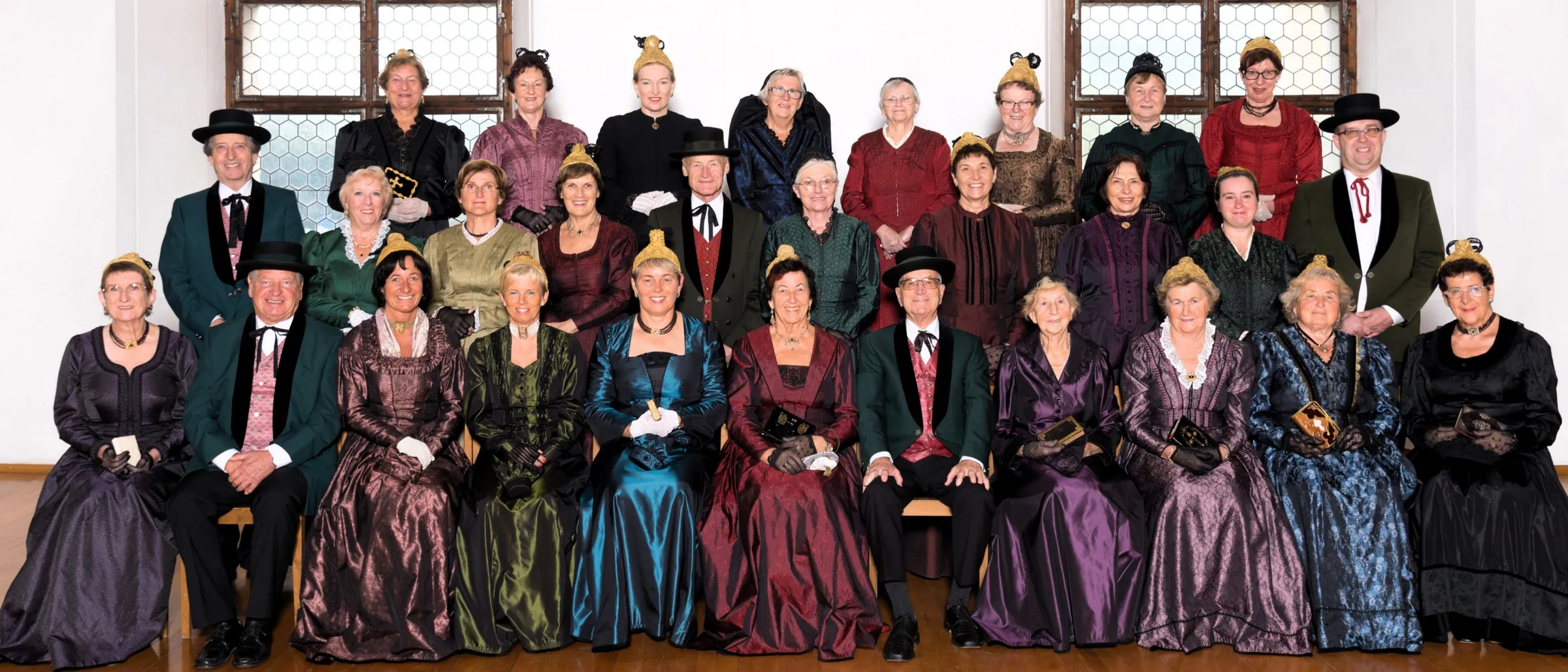 Eine Gruppe von Erwachsenen, die in historischen Kostümen gekleidet sind, wahrscheinlich für eine historische Nachstellung, posieren für ein Foto. Die Kostüme variieren in Farbe und Stil, und einige tragen Hüte.