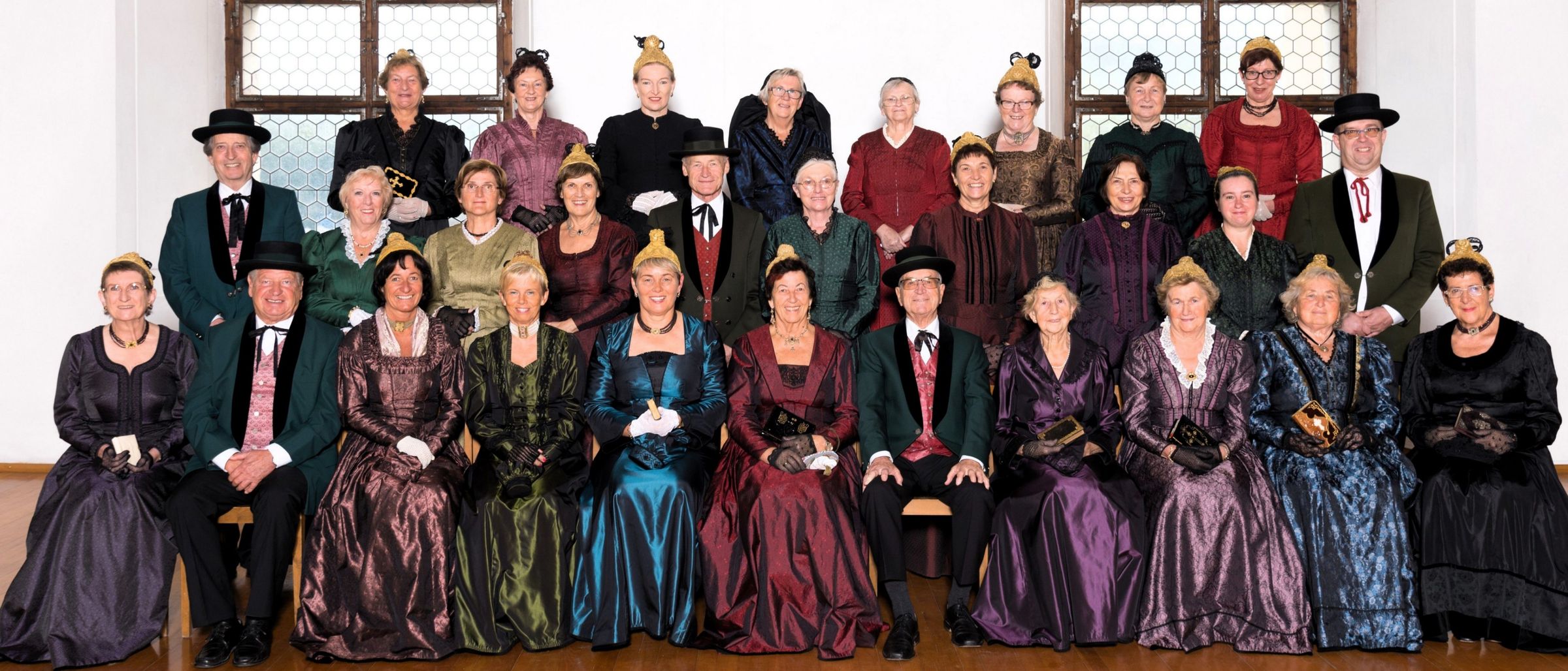 Eine Gruppe von Erwachsenen, die in historischen Kostümen gekleidet sind, wahrscheinlich für eine historische Nachstellung, posieren für ein Foto. Die Kostüme variieren in Farbe und Stil, und einige tragen Hüte.