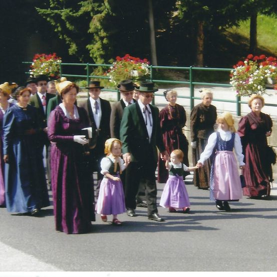 Eine Gruppe von Menschen in traditioneller Kleidung geht auf einer Straße, wobei zwei junge Mädchen Händchen halten.