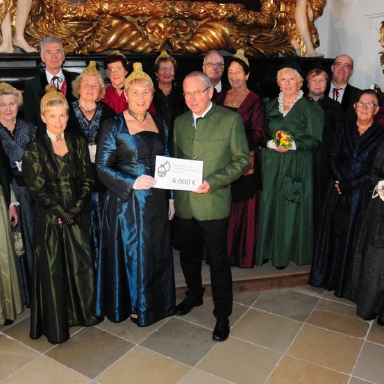 Eine Gruppe von Menschen in historischen Kostümen posiert für ein Foto, wobei ein Mann einen Scheck über 4.000 Euro hält.