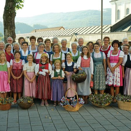 Eine Gruppe von Menschen in traditioneller Kleidung, einige mit Blumenkörben, posiert für ein Foto vor einer Kirche.