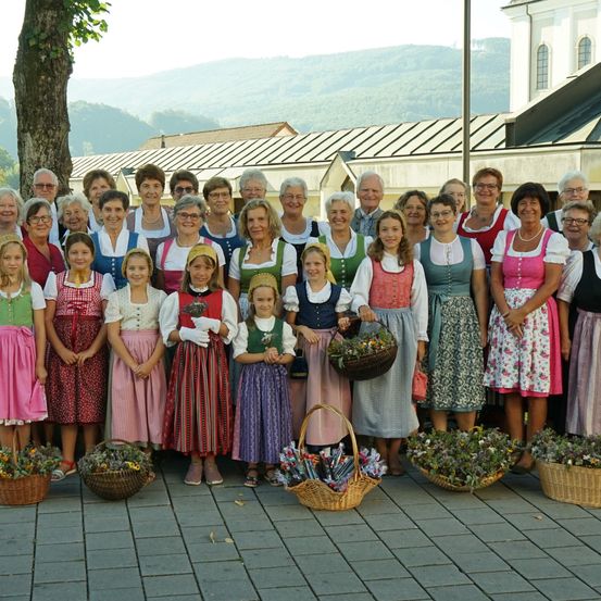 Eine Gruppe von Menschen in traditioneller Kleidung, einige mit Blumenkörben, posiert für ein Foto vor einer Kirche.