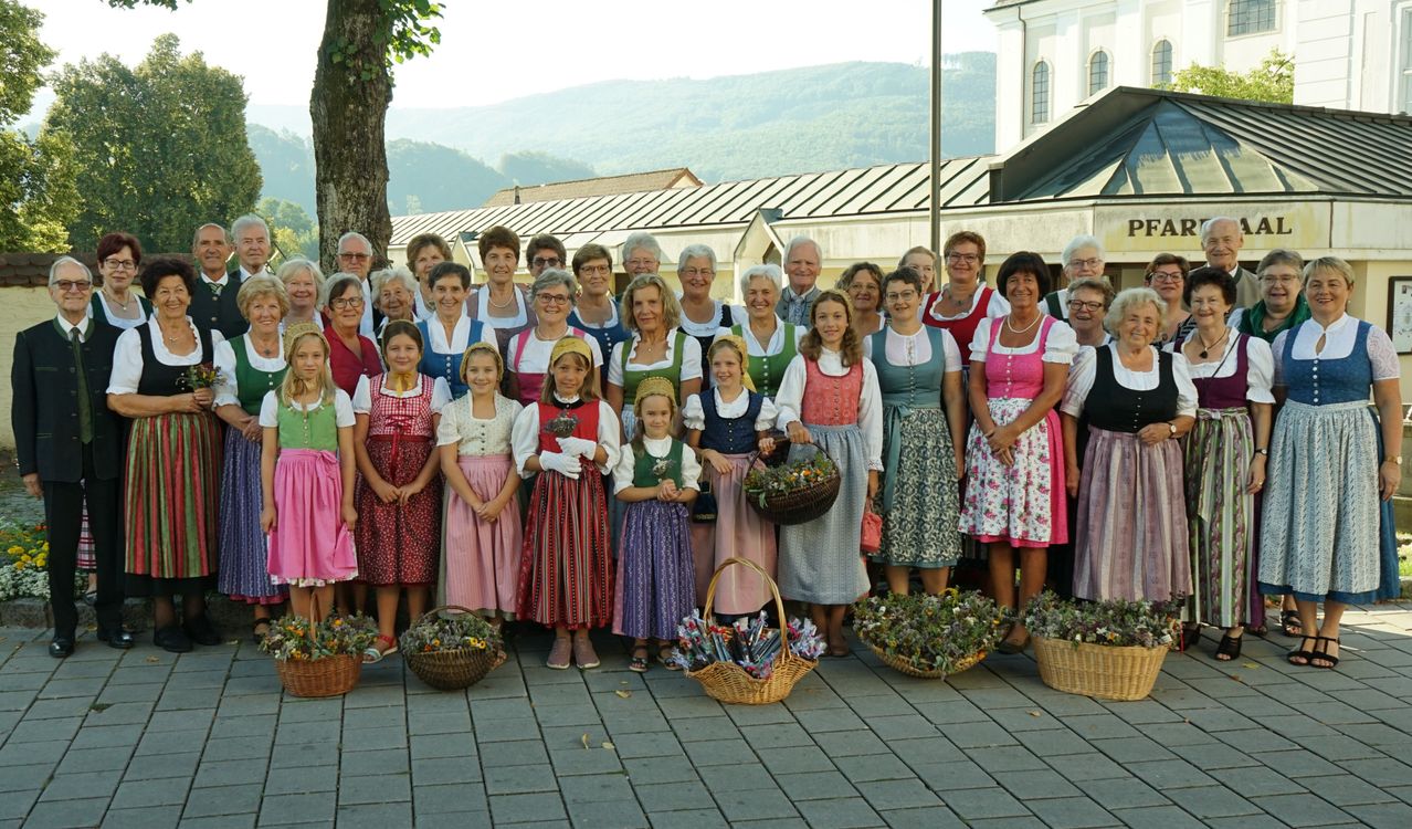 Eine Gruppe von Menschen in traditioneller Kleidung, einige mit Blumenkörben, posiert für ein Foto vor einer Kirche.