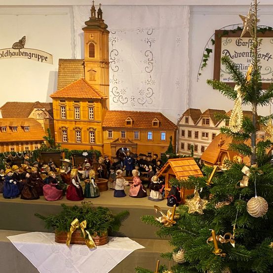Eine Weihnachtsausstellung mit einer Miniatur-Dorfszene, einem geschmückten Weihnachtsbaum und einer Menschenmenge in historischen Kostümen.