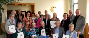 Eine Gruppe älterer Personen ist für eine Versammlung in einem Raum versammelt. Sie halten Papiere mit dem Wort NEIN darauf.