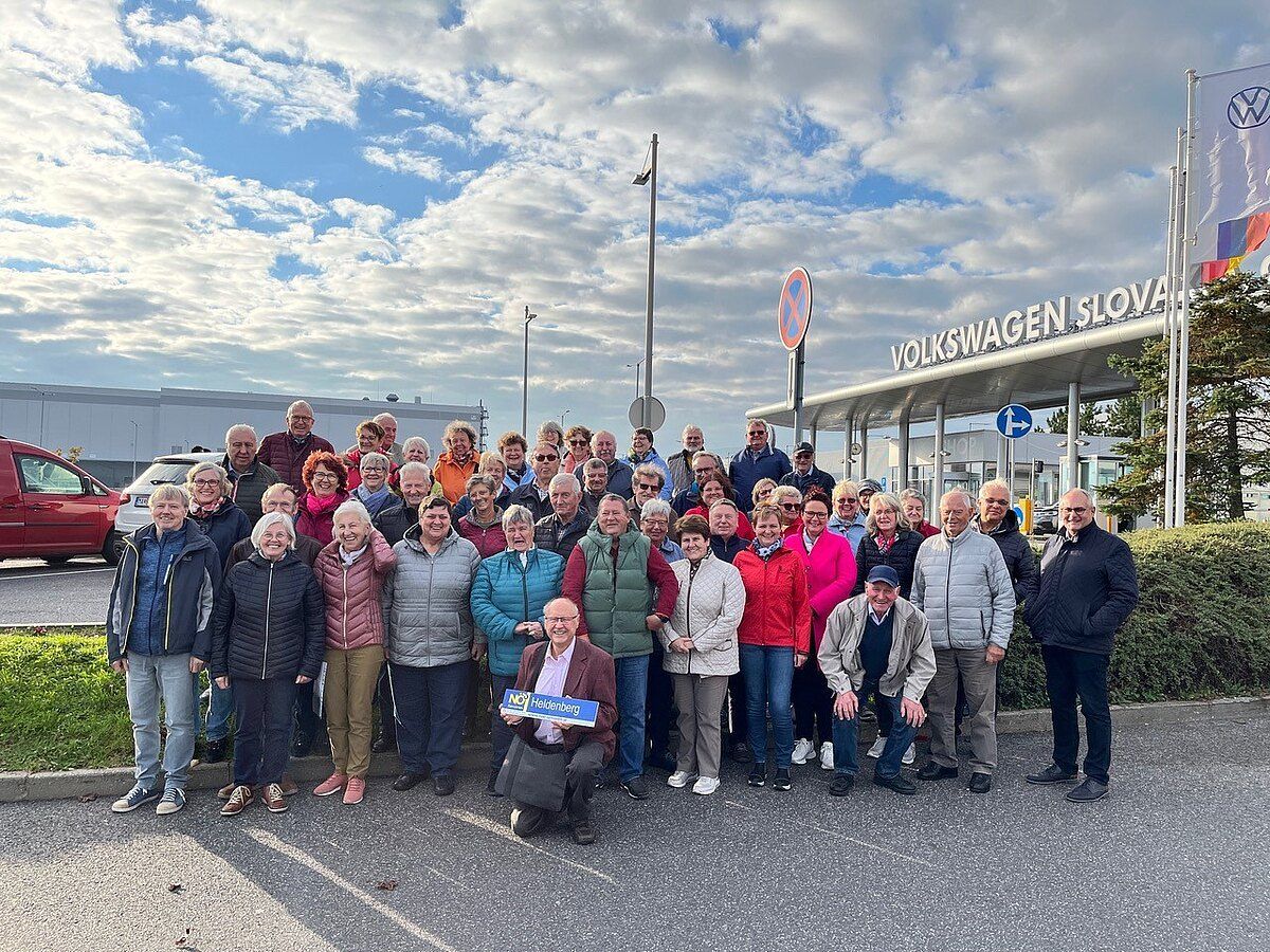 Eine Gruppe von Menschen posiert für ein Foto vor der Volkswagen Slowen Fabrik. Sie tragen Winterkleidung. Einige von ihnen halten Plakate.