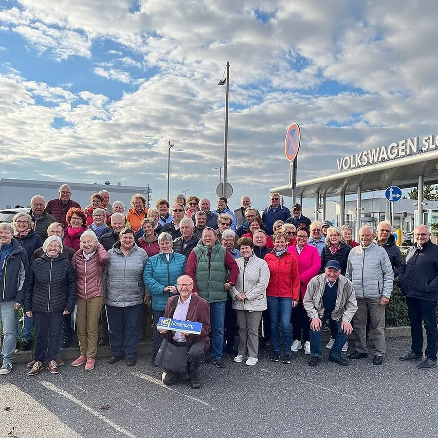 Eine Gruppe von Menschen posiert für ein Foto vor der Volkswagen Slowen Fabrik. Sie tragen Winterkleidung. Einige von ihnen halten Plakate.