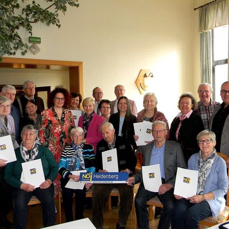 Eine Gruppe von Menschen in einem Raum, einige sitzend und andere stehend, halten weiße Papiere mit dem Wort NO darauf. Sie scheinen für ein Foto zu posieren.