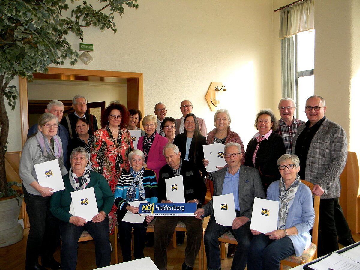 Eine Gruppe von Menschen in einem Raum, einige sitzend und andere stehend, halten weiße Papiere mit dem Wort NO darauf. Sie scheinen für ein Foto zu posieren.