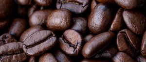 Eine Nahaufnahme eines Haufens gerösteter Kaffeebohnen, dunkelbraun mit sichtbaren Texturen und Rissen.