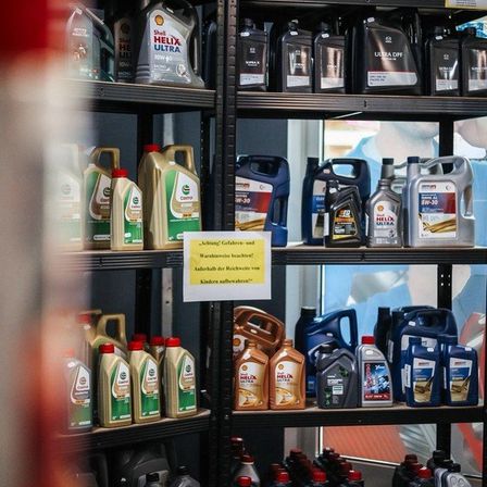 Regale mit Motoröl in einem Geschäft mit Warnschildern für Kinder und Vorsicht. Verschiedene Marken und Größen von Ölbehältern sind ausgestellt.