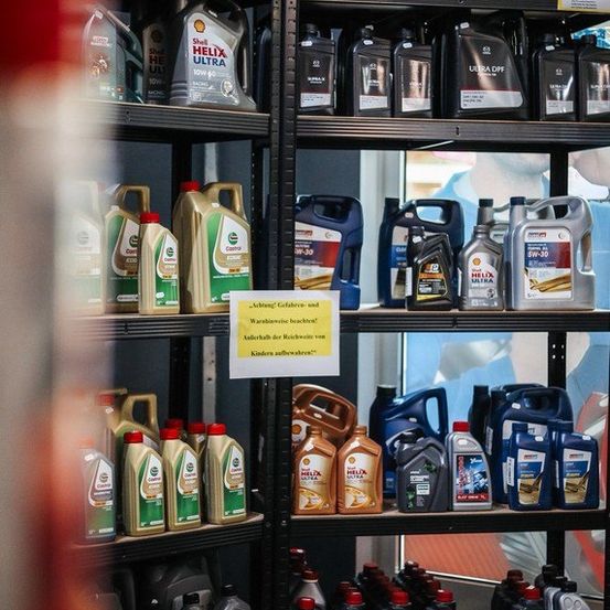 Regale mit Motoröl in einem Geschäft mit Warnschildern für Kinder und Vorsicht. Verschiedene Marken und Größen von Ölbehältern sind ausgestellt.