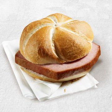 Ein Sandwich mit zwei Scheiben Schinken auf einem weißen Papiertuch auf einer weißen Oberfläche.
