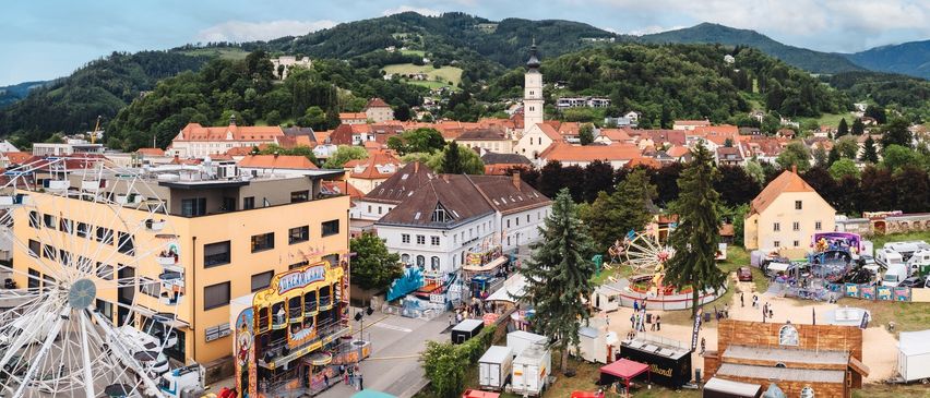 Luftaufnahme einer Stadt mit einem Jahrmarkt und einer Kirche in der Ferne.