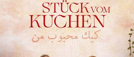 Ein Paar sitzt auf einer Bank vor einer Wand mit den Worten 'Stuck vom Kuche' und einem arabischen Satz. Die Frau lächelt und der Mann schaut sie an. Eine Lampe ist links.