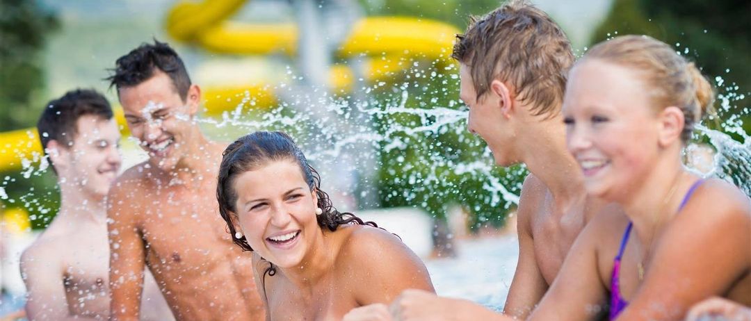 A group of young adults are enjoying themselves in a water park, with water splashing around them. They are smiling and appear to be having a good time.