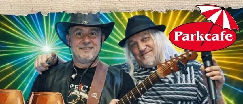 Zwei Männer spielen bei einem Musikevent. Einer spielt Gitarre und der andere hält ein Mikrofon. Es gibt eine Schüssel mit Kastanien, zwei Weingläser und ein roter Regenschirm im Bild.