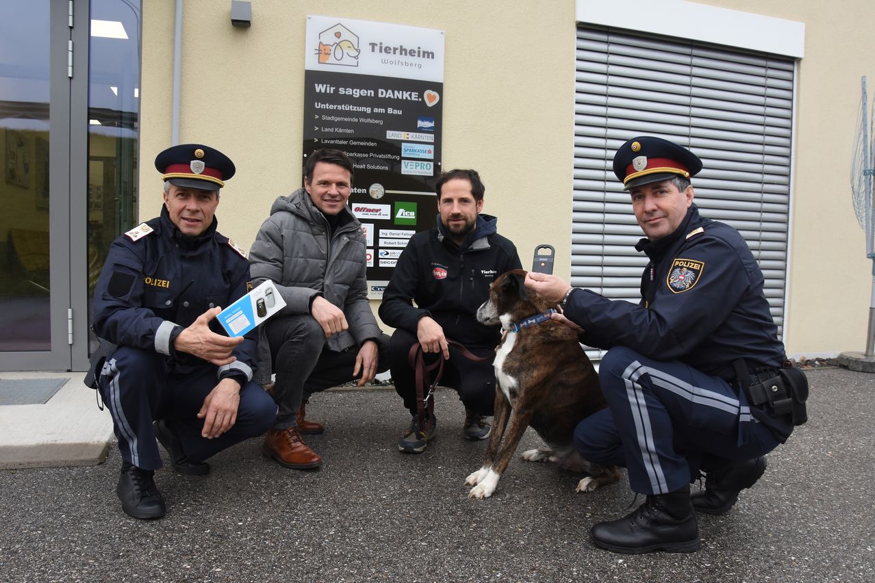 Vier Polizeibeamte und ein Hund posieren für ein Foto vor einem Gebäude mit einem Schild, das 'Tierheim Wolfsberg' besagt.