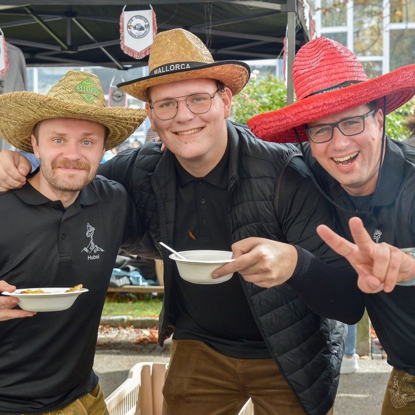 Drei Männer in Strohhüten posieren für ein Foto, wobei einer der Männer ein Friedenszeichen macht und die anderen beiden weiße Schüsseln halten.