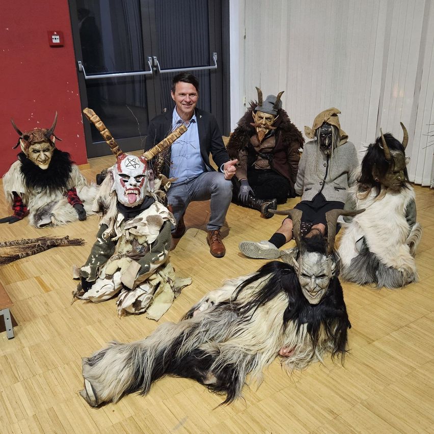 Eine Gruppe von Personen in Ziegenmasken und Hörnern, die ein Foto mit einem Mann in formaler Kleidung machen.