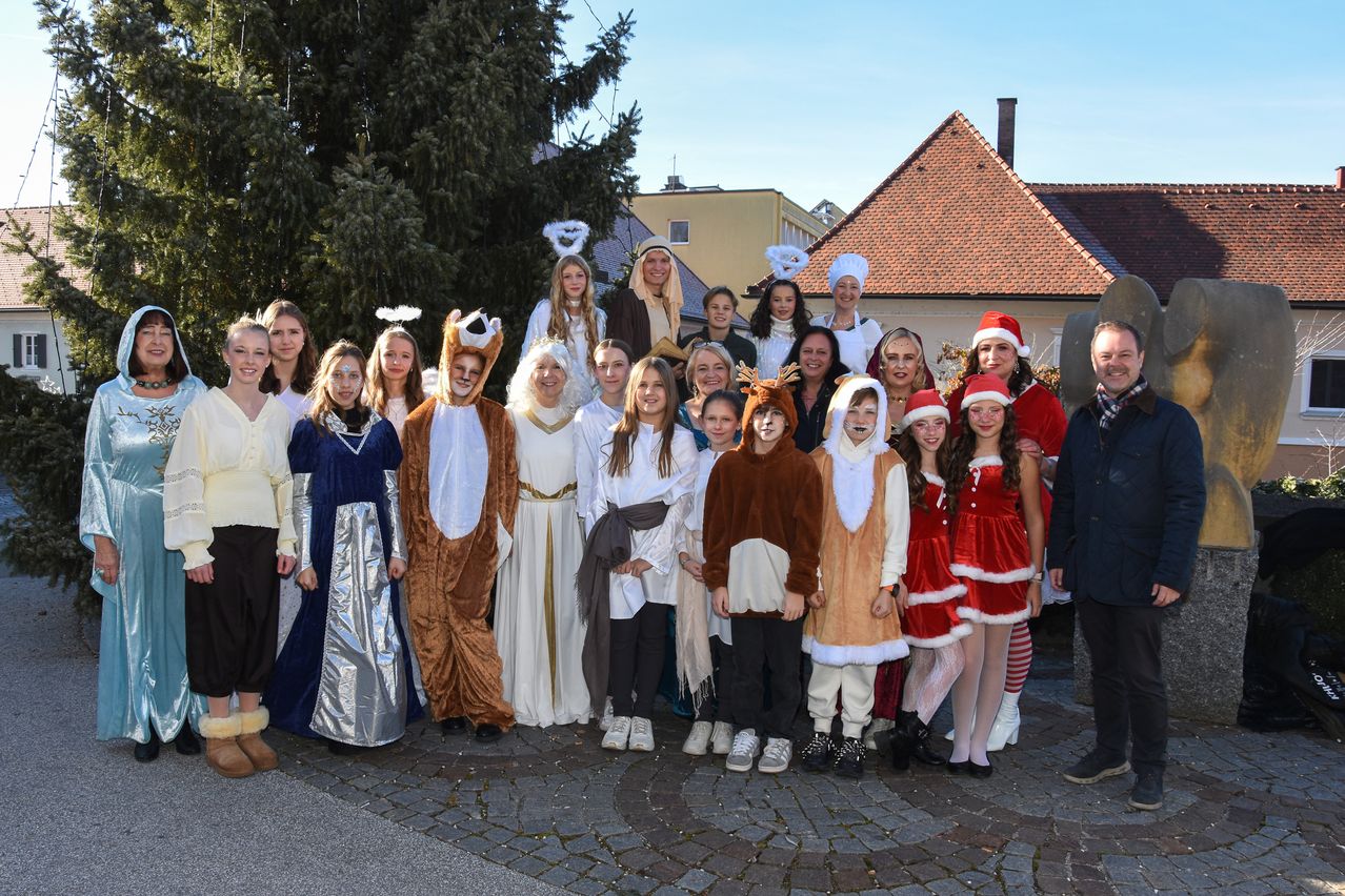 Eine Gruppe von Personen in verschiedenen Kostümen, darunter Engel, Tiere und der Weihnachtsmann, posiert für ein Foto vor einem Gebäude.