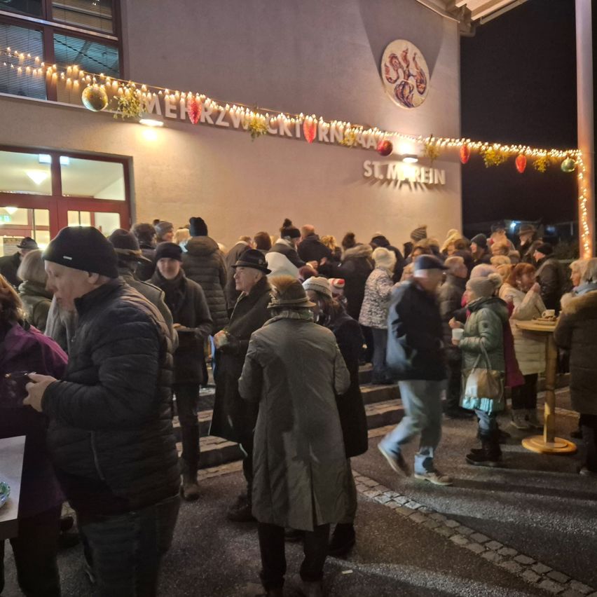 Bei Nacht stehen eine Menschenmenge vor einem Gebäude mit festlichen Lichtern, möglicherweise warten sie in einer Schlange. Das Gebäude ist mit St. Martin beschriftet.