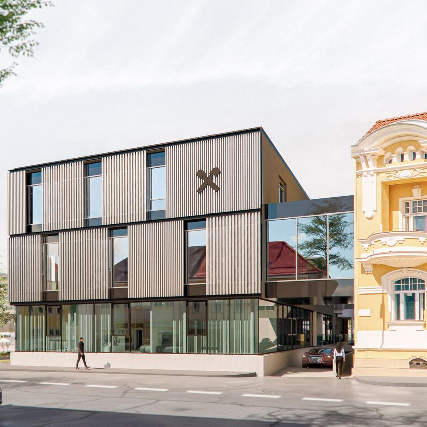 Ein modernes Gebäude mit gestreifter Fassade steht neben einem traditionellen gelben Gebäude. Eine Person läuft vor dem modernen Gebäude.