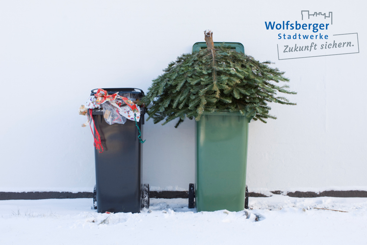 Zwei Mülltonnen auf schneebedecktem Boden, eine mit einem Weihnachtsbaum, die andere mit eingepackten Geschenken, vor einer weißen Wand.