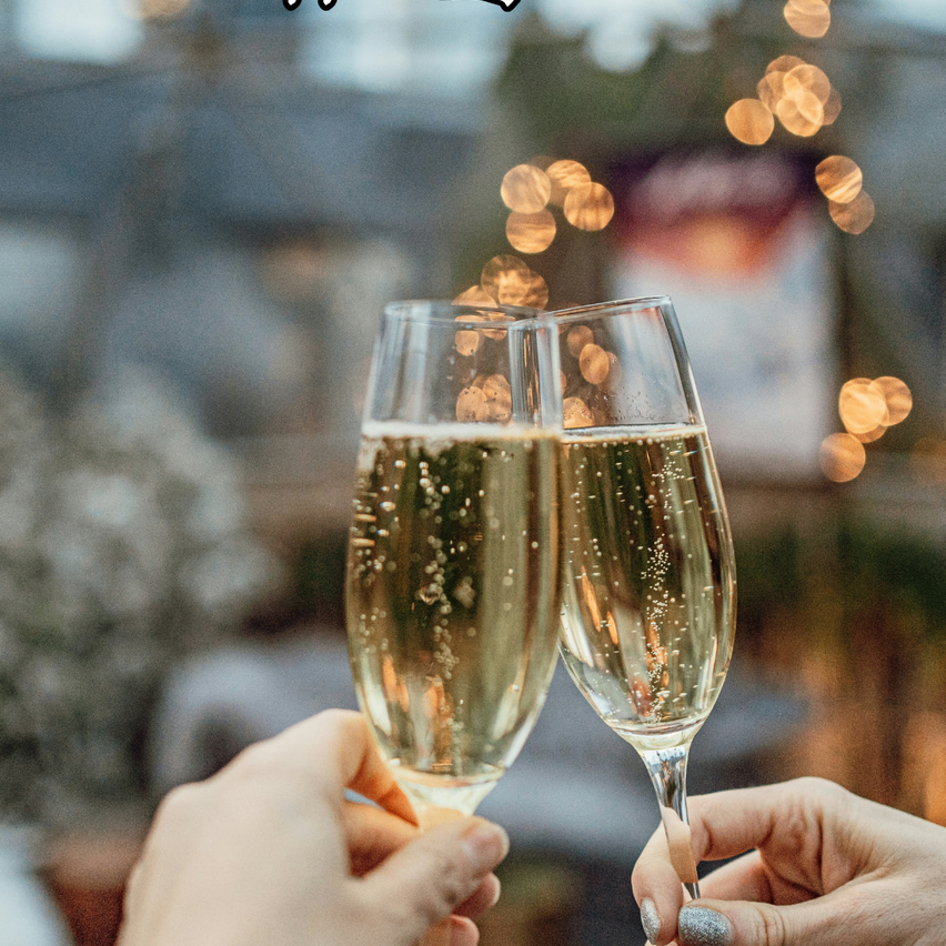 Zwei Hände halten Weingläser mit Champagner gefüllt, funkelnd mit Blasen, beleuchtet von festlichen Lichtern im Hintergrund.