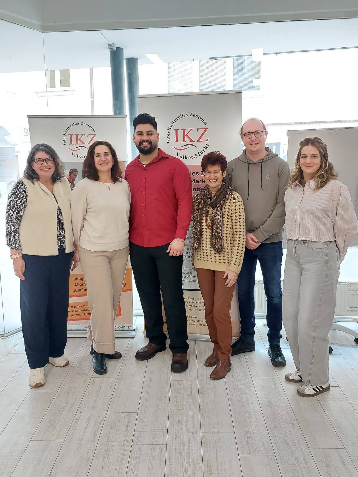 Fünf Erwachsene, zwei Frauen und drei Männer, stehen zusammen vor Bannern mit 'IKZ' und 'Volker.Markt' darauf. Sie scheinen für ein Foto zu posieren.
