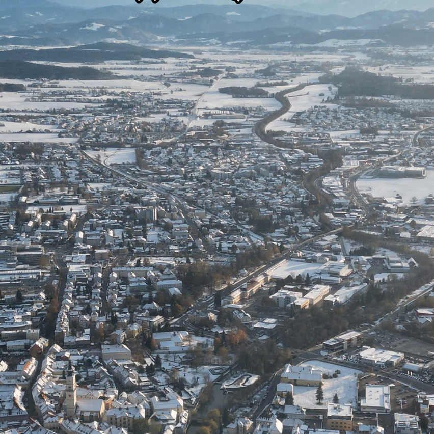 Luftaufnahme einer schneebedeckten Stadt. Gebäude, Straßen und Berge sind sichtbar. Der Himmel ist klar.