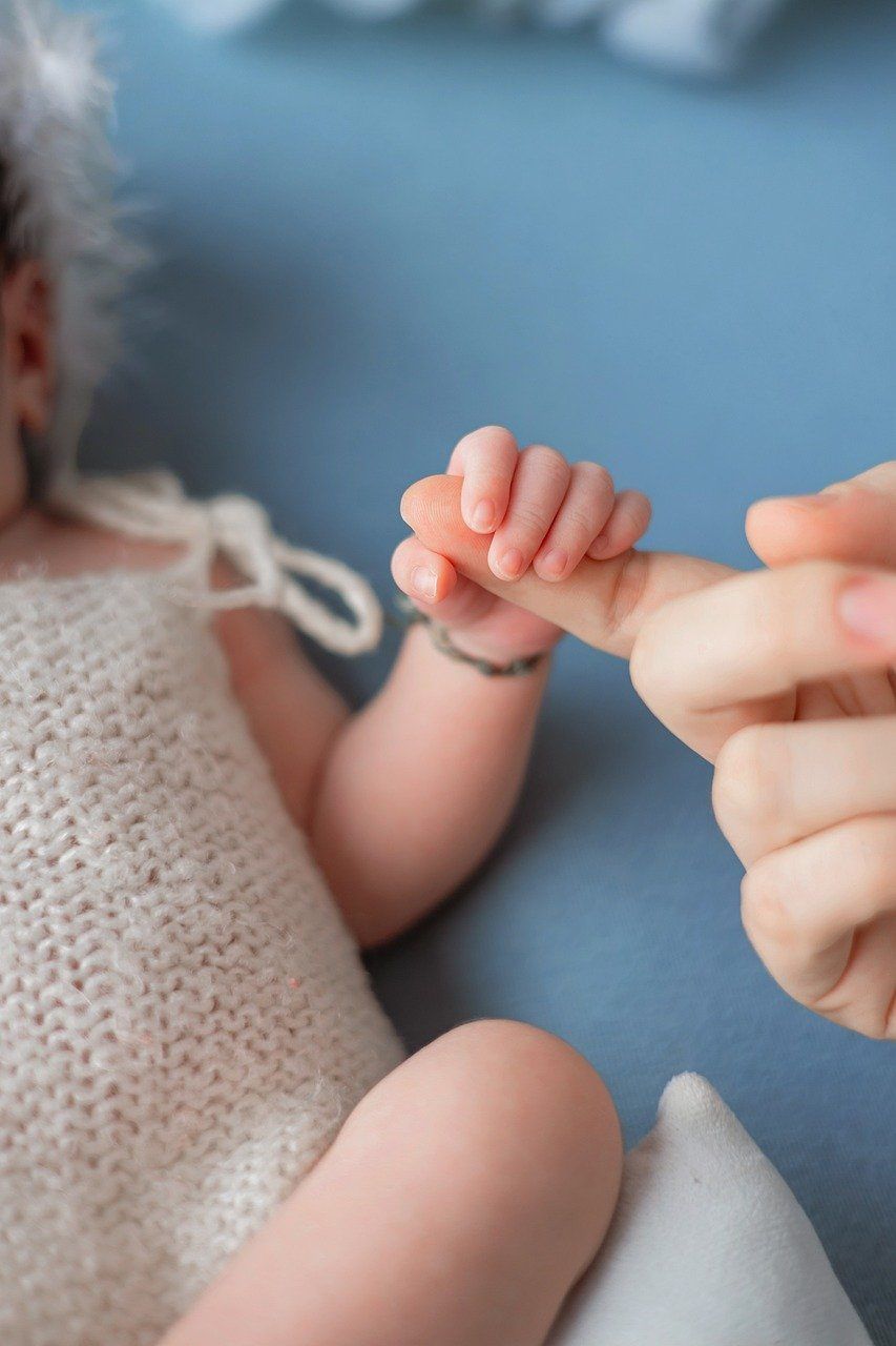 Eine Person hält die winzige Hand eines Neugeborenen und zeigt eine enge Bindung. Das Baby trägt ein gestricktes Outfit mit einem Armband.