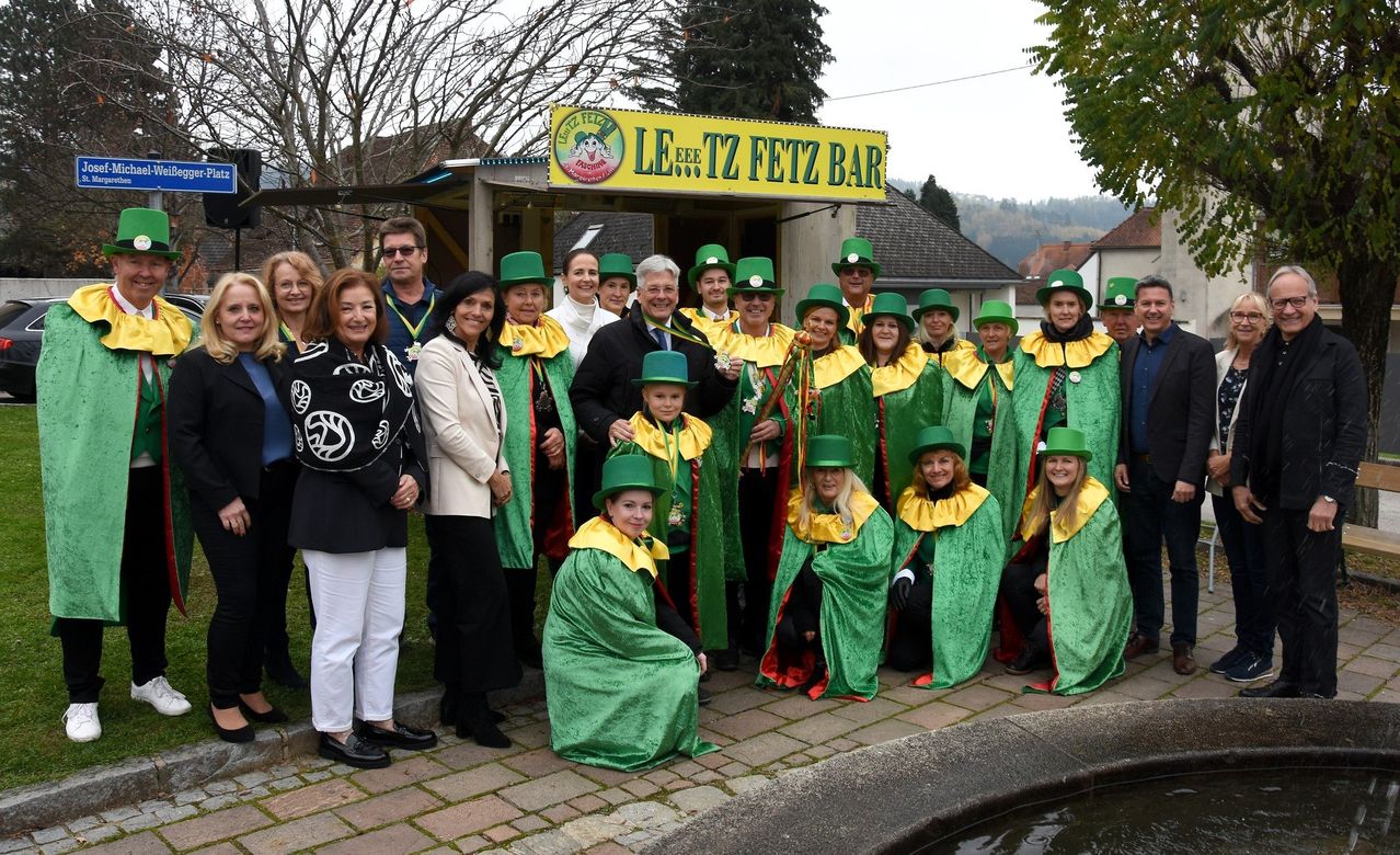 Eine Gruppe von Menschen in grünen Kostümen und Hüten posiert für ein Foto vor einem Schild für Leitz Fetz Bar.