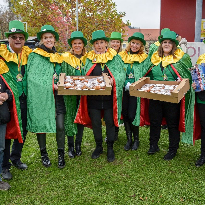Eine Gruppe von Menschen in grünen Hüten und Roben posiert für ein Foto und hält Schachteln mit Gebäck auf einem Rasen.