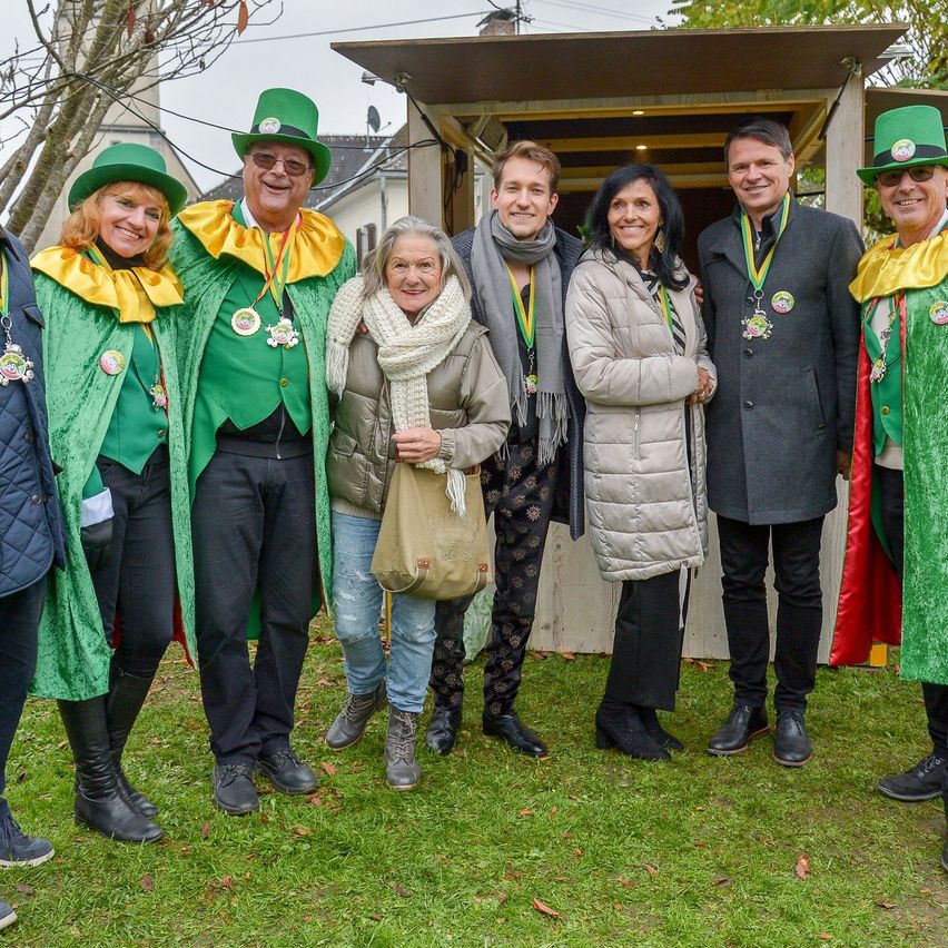 Eine Gruppe von Menschen in grünen Kostümen mit Medaillen steht vor einem Haus mit einem Baum im Hintergrund.