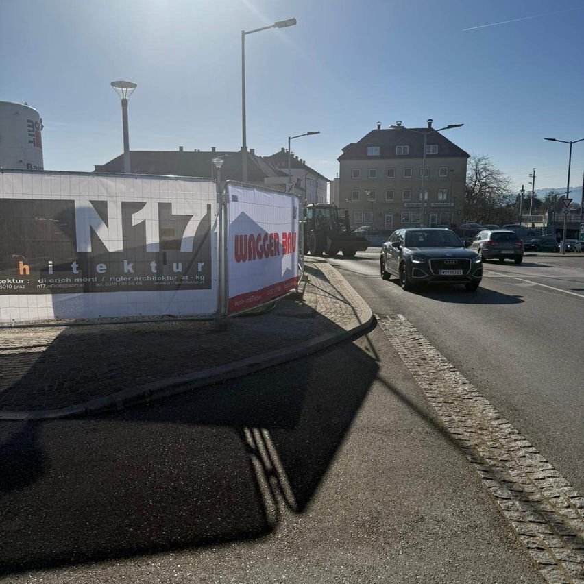 A street with a black Audi car driving, buildings, streetlights, and a construction banner with the text Netz Architektur.