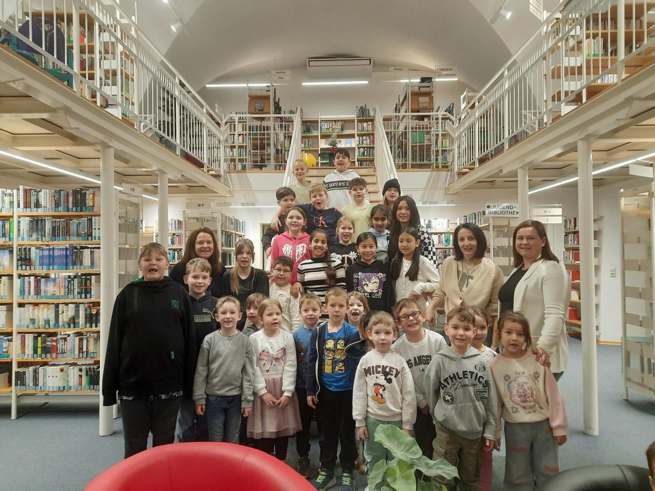 Eine Gruppe von Kindern und Erwachsenen in einer Bibliothek. Die Kinder lächeln und posieren für ein Foto.