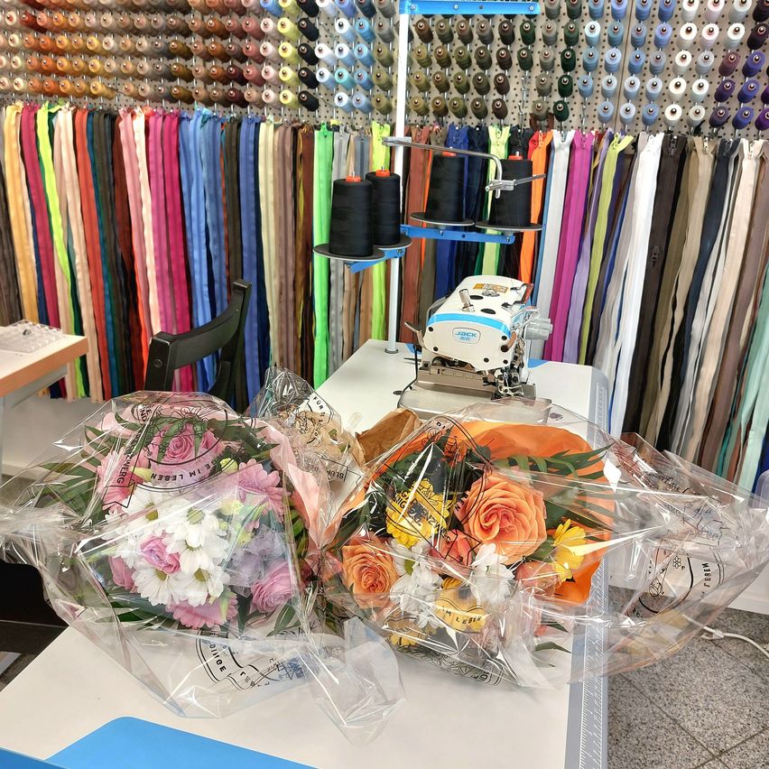 A table with two bouquets of flowers in clear plastic bags sits in front of a wall full of colorful spools of thread.