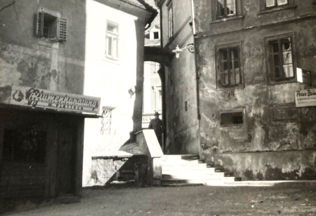 Black and white photo of a man standing in a narrow alley between two old buildings.