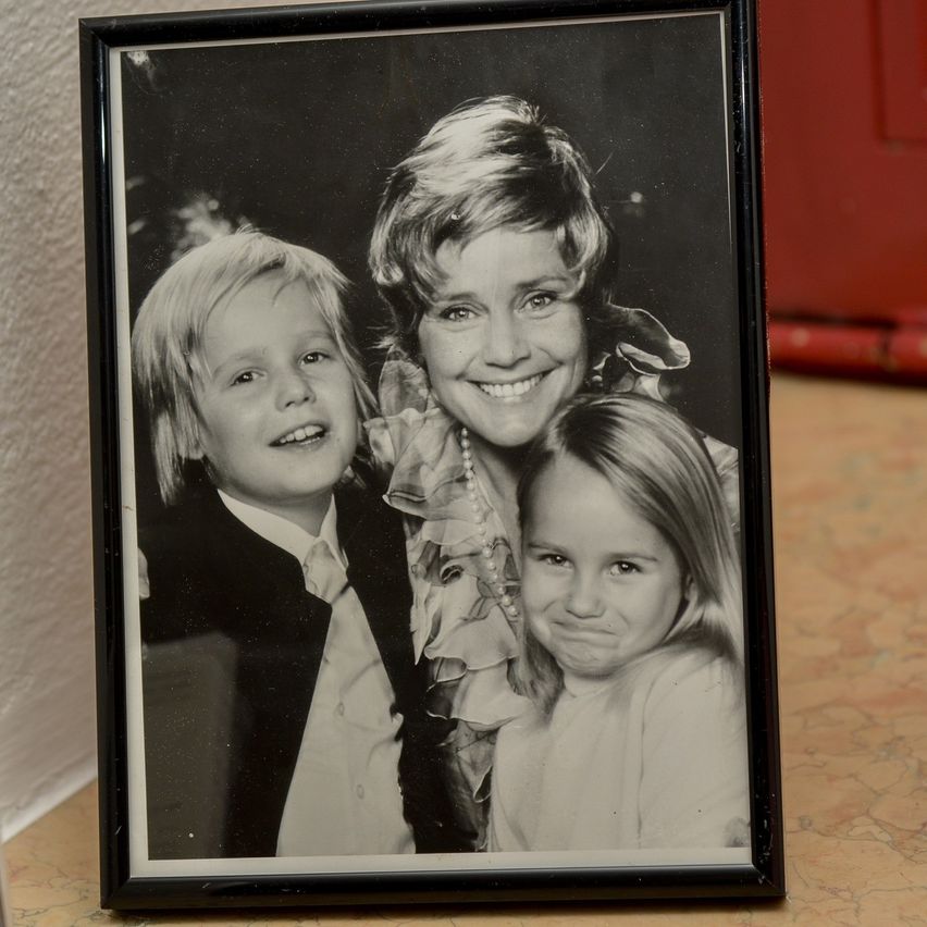 Ein gerahmtes Schwarz-Weiß-Foto einer Frau und zwei Kindern, die in die Kamera lächeln. Die Frau trägt eine Perlenkette.