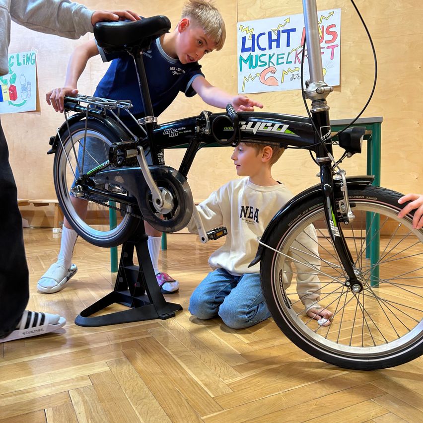 Zwei Jungen untersuchen ein schwarzes Fahrrad mit dem Wort Cygo darauf. Ein Junge hält das Lenker, der andere kniet und schaut auf das Vorderrad.