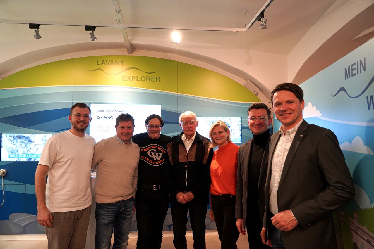 Five individuals are standing in a room with a banner labeled 'Lavant Explorer'. They are smiling and seem to be posing for a photo.