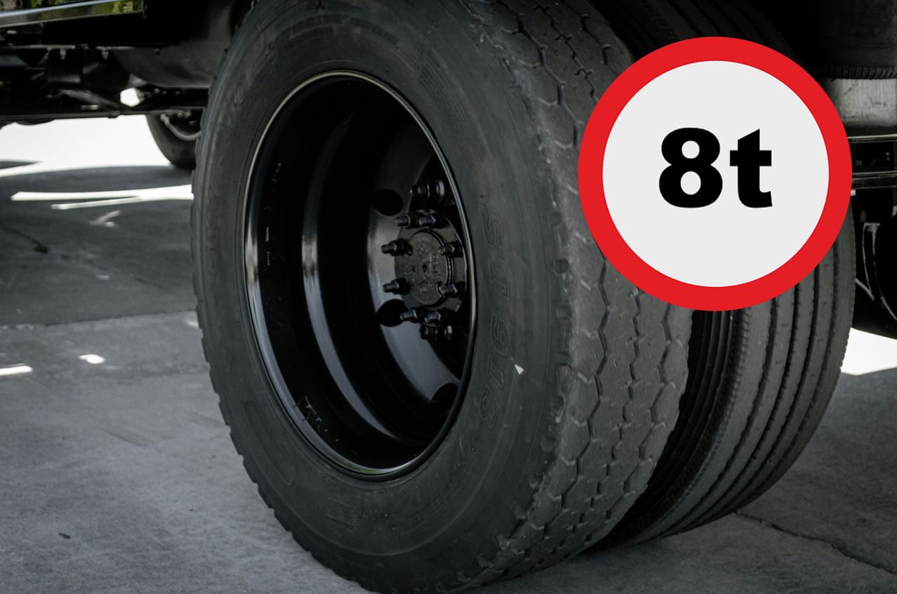 Nahaufnahme eines schwarzen Reifens eines Fahrzeugs mit einem roten und weißen Schild, das 8t anzeigt. Der Reifen ist auf einem silbernen Leichtmetallrad montiert.