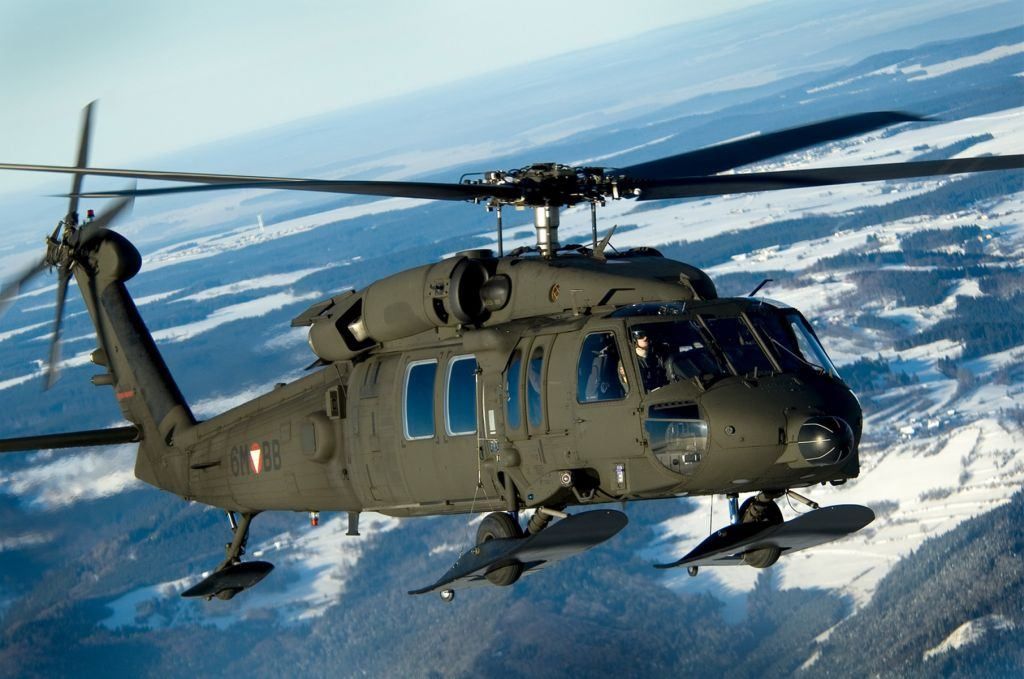 A military helicopter with the number 61-8B on its side is flying over a snowy landscape.